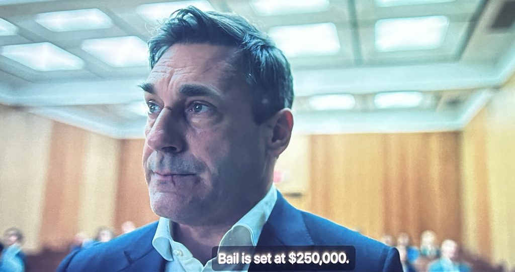 Screen capture from Your Friends & Neighbors season 1 episode 8 showing Andrew Cooper, portrayed by Jon Hamm, in a courtroom, close-up of his face with visible facial bruising and cuts, wearing a dark suit and white shirt, seated spectators blurred in the background, subtitle text at the bottom reading βBail is set at $250,000.β
Alt text by ALT Text Artist GPT