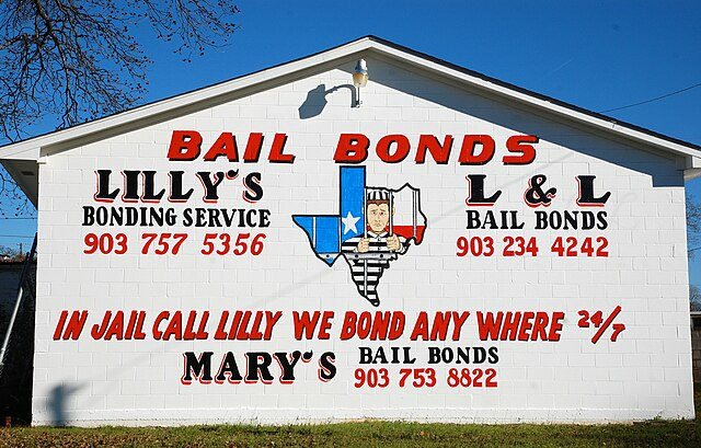 White brick building facade with painted bail bond advertising. The top text reads "Bail Bonds". On the left, the text reads "Lillyβs Bonding Service" with a phone number. On the right, the text reads "L & L Bail Bonds" with another phone number. At the center, an illustration shows the outline of Texas with a person behind jail bars. Across the middle, the text reads "In jail call Lilly we bond any where 24/7." At the bottom, the text reads "Maryβs Bail Bonds" with a phone number.